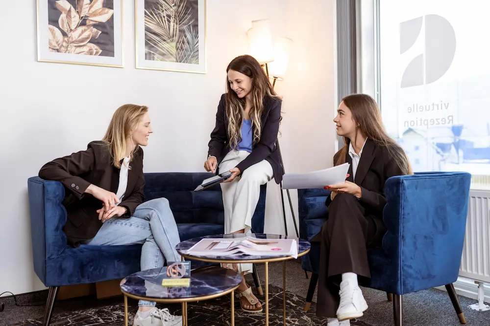Drei Personen, die in einem modernen Büro sitzen, arbeiten an einem Projekt und diskutieren Unterlagen. Die Frauen tragen formelle Kleidung und arbeiten an der Optimierung von Geschäftsprozessen.