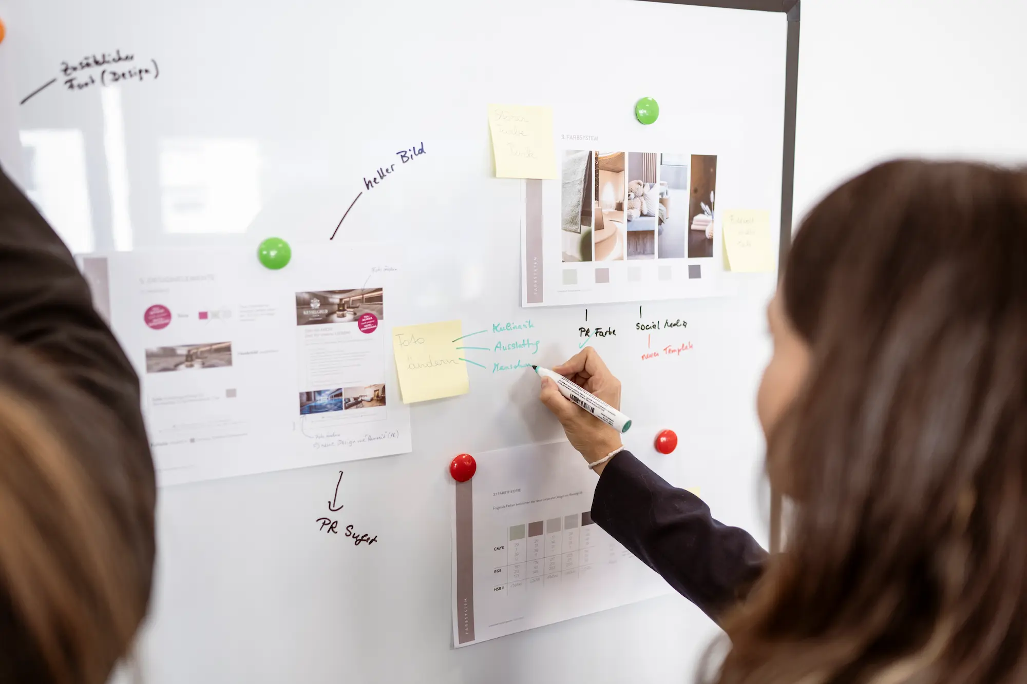 Eine Mitarbeiterin von globboard schreibt auf ein Whiteboard, das mit bunten Haftnotizen und Druckmaterialien bedeckt ist. Sie arbeitet an einer Marketingstrategie.