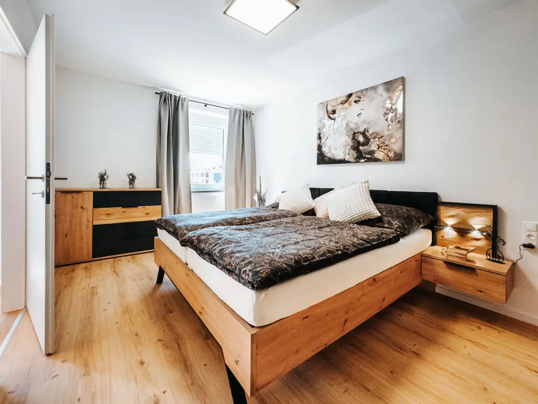 Modernes Schlafzimmer im Apartment Grand Prix Spielberg by globboard in Zeltweg, Österreich. Das Zimmer bietet eine komfortable Atmosphäre mit einem Doppelbett, einem Nachttisch und stilvollen Möbeln – ideal für einen Aufenthalt in der Nähe des Red Bull Rings.